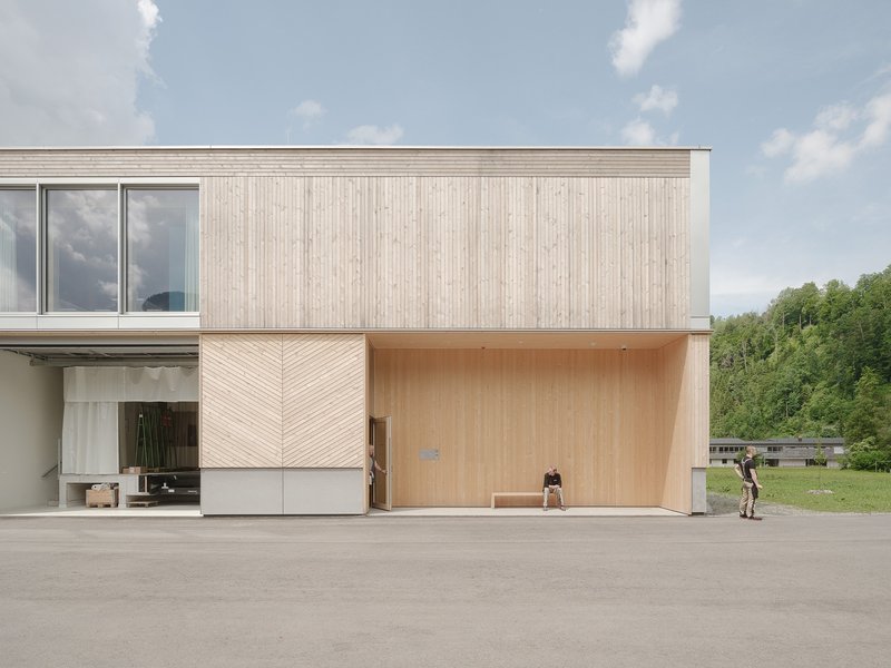 Two-story facade combining vertical timber cladding with herringbone wood panels and a recessed workshop opening
