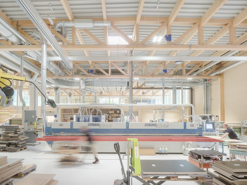 Fabrication workshop with exposed timber beam ceiling and CNC machinery with workers in motion