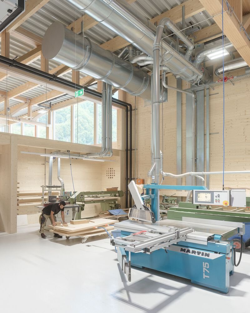 Workshop interior showing exposed ventilation ducts and panel saw equipment beneath timber structure