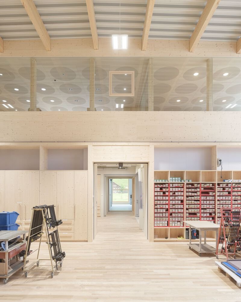 Two-story workspace with glass partitions and material storage shelving under cross-laminated timber beams