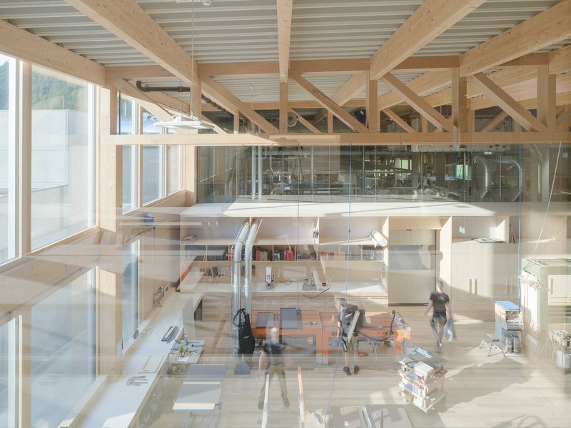 Double-height workspace with timber frame and glass-enclosed mezzanine overlooking ground floor workstations