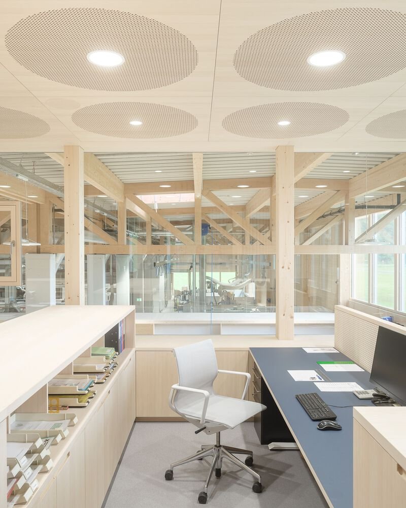 Office area with perforated circular ceiling panels and workstation beneath timber beam structure