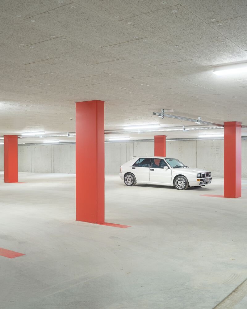 Underground parking garage with red square columns and a white car under fluorescent lighting
