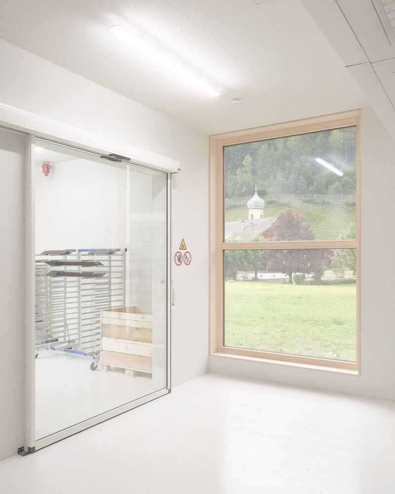 White room with timber-framed window overlooking a green lawn and church beyond a glass door
