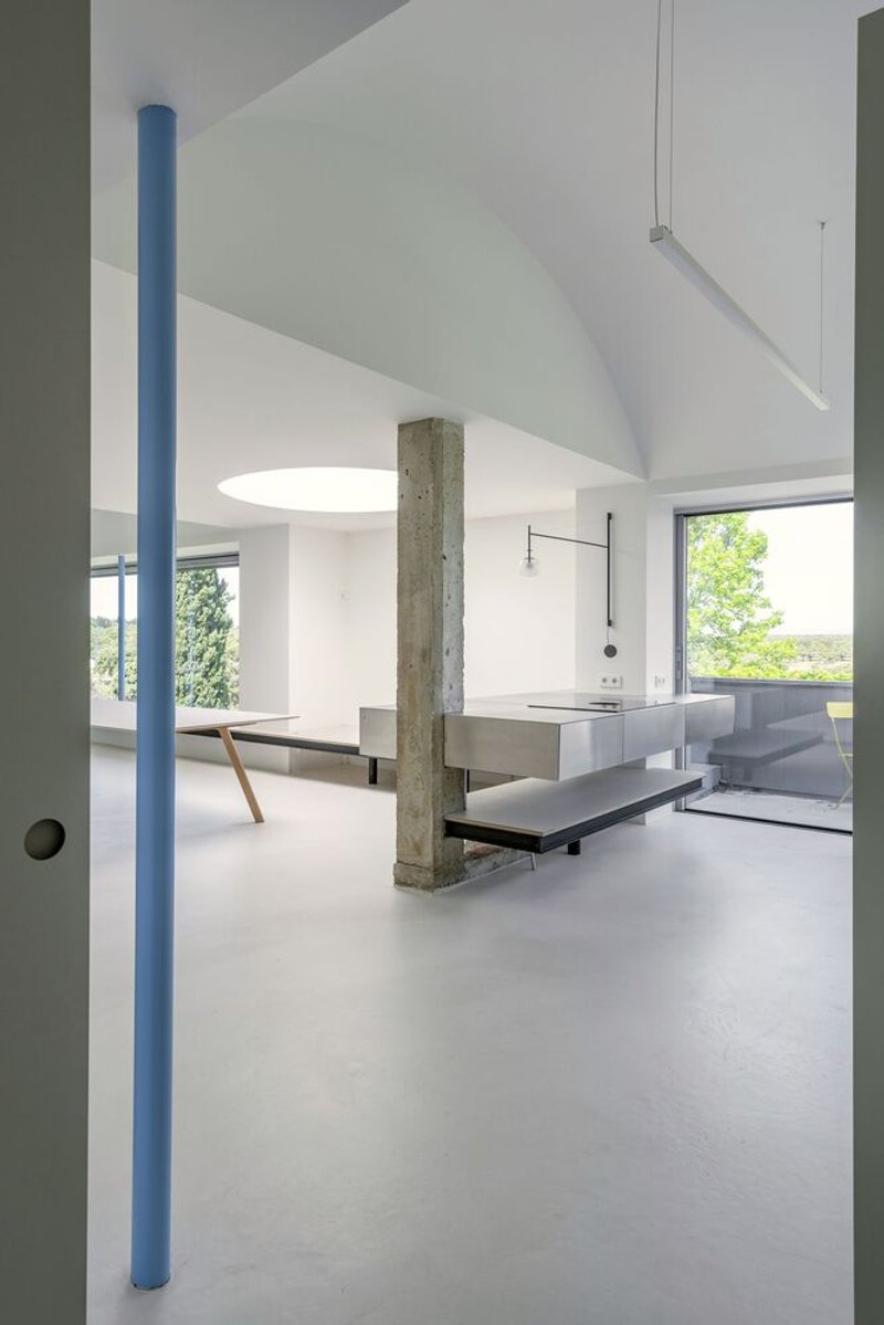 Living space with blue steel columns, concrete pillar, and suspended linear lighting fixture overhead