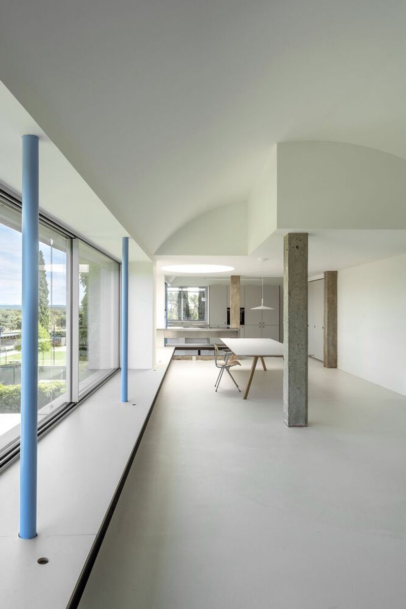 Open interior with vaulted ceiling, exposed concrete columns, and continuous glazing overlooking green landscape