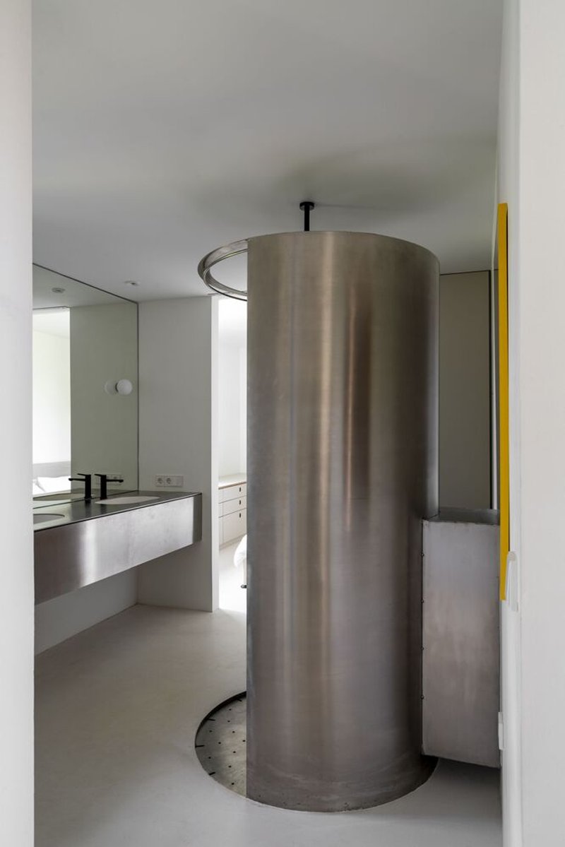 Cylindrical stainless steel shower enclosure with ceiling-mounted circular ring and perforated base in a white bathroom