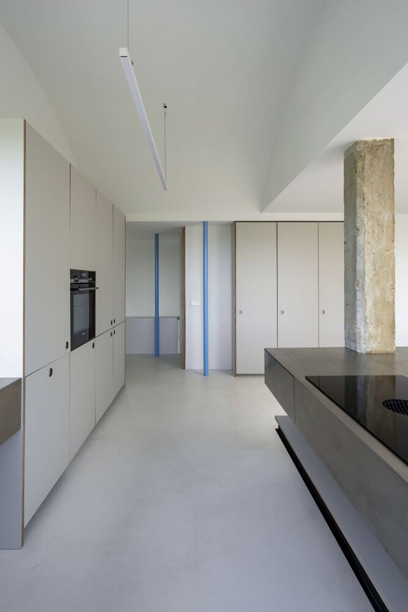 Kitchen corridor with pale cabinetry, blue columns, and linear pendant light under vaulted ceiling