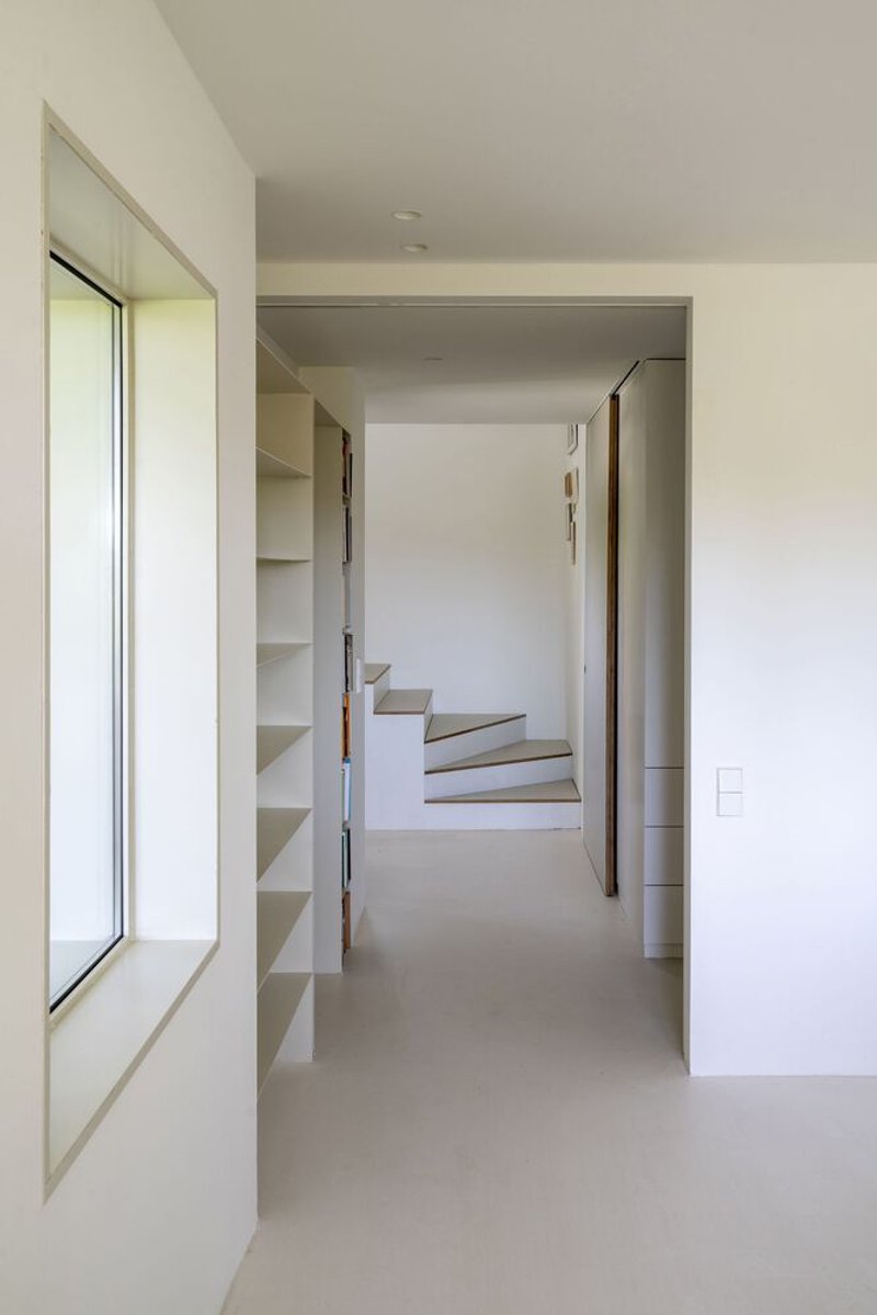 Hallway with built-in shelving leading to a staircase with timber handrail and angled steps