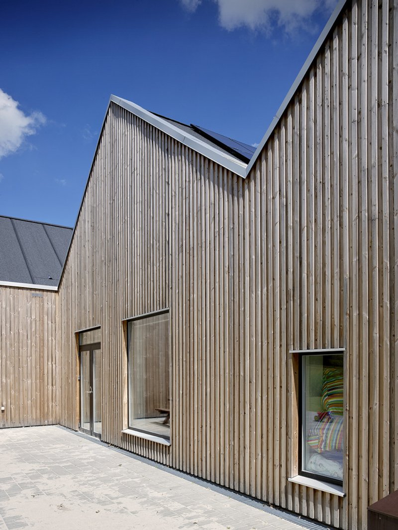 Vertical timber cladding facade with narrow ribbon windows and a recessed doorway under a clear sky