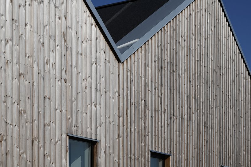 Detail of vertical timber cladding at gable ridge with two small windows and black-framed skylight above