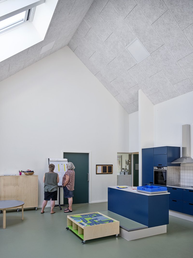 Open-plan interior with blue kitchen island, acoustic ceiling tiles and two children working at a wall-mounted desk