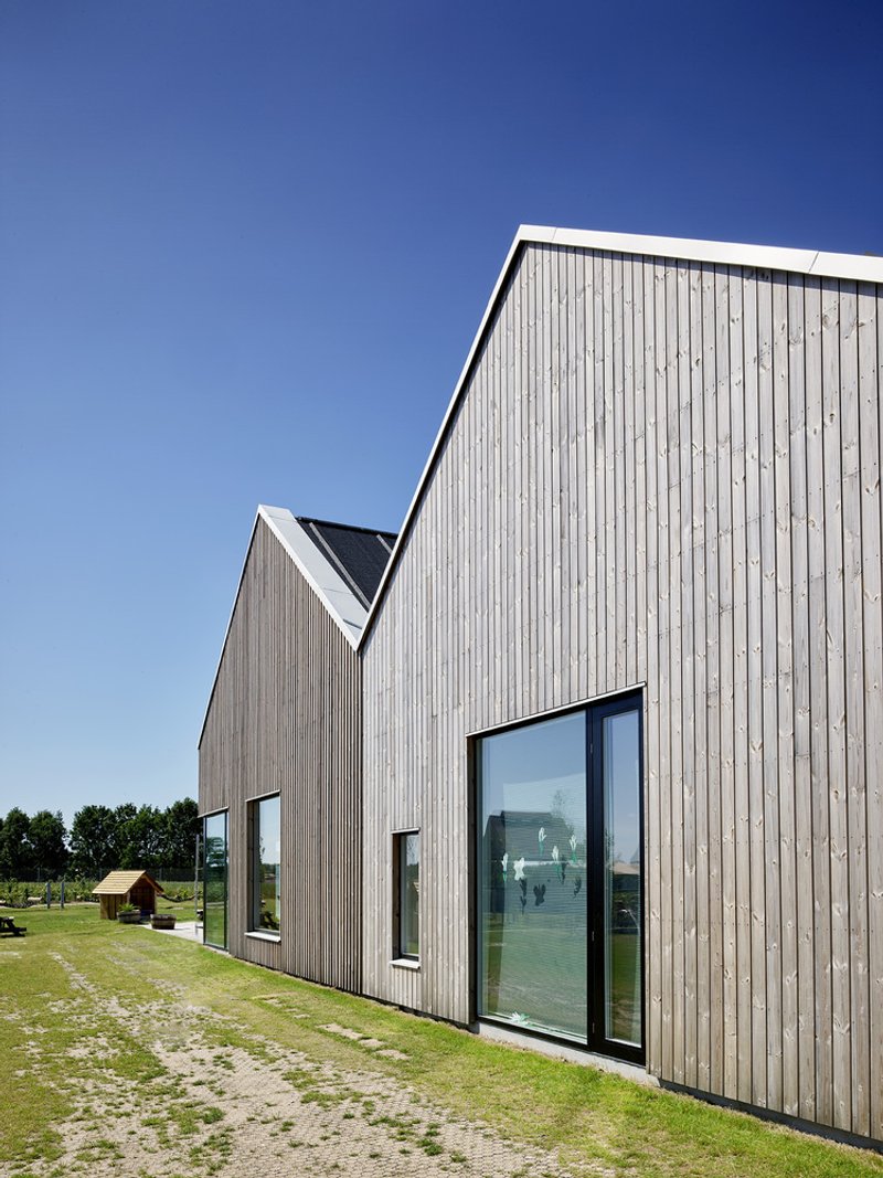 Vertical timber cladding with narrow windows on gabled end wall under clear blue sky