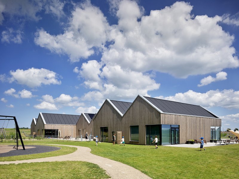 View of gabled timber structures across mown grass with children and adults scattered along the pathway