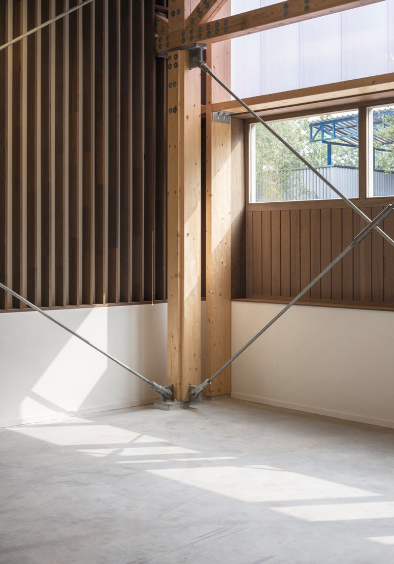 Corner detail of timber column with diagonal steel cross-bracing in sunlit interior space