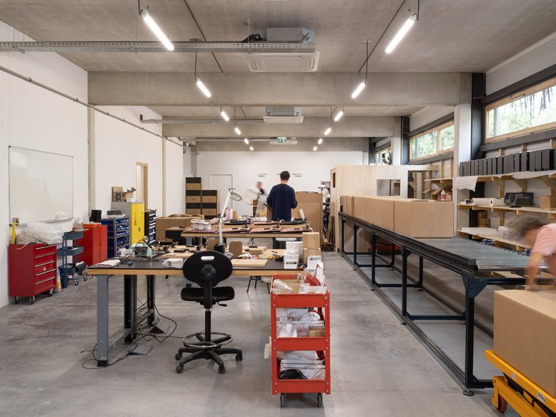 Workshop space with people moving past workbenches loaded with materials and cardboard samples