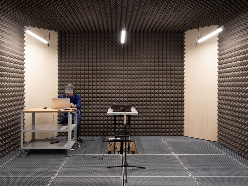 Sound testing chamber lined with pyramidal acoustic foam panels and a person examining equipment at a workbench