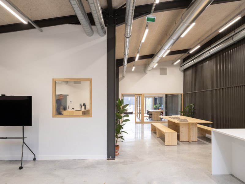 Interior corridor view through timber-framed openings with polished concrete floors and a potted plant in terracotta