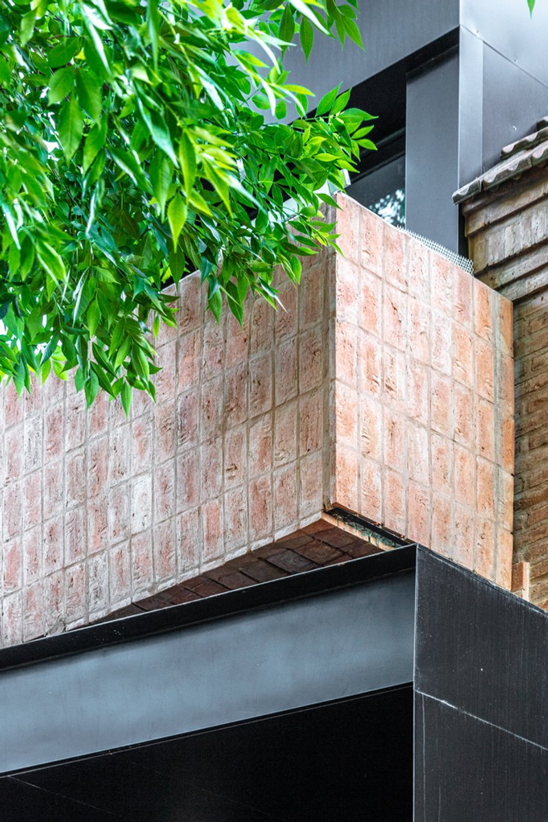 Reclaimed brick planter box with steel frame and overhanging foliage against a gray facade