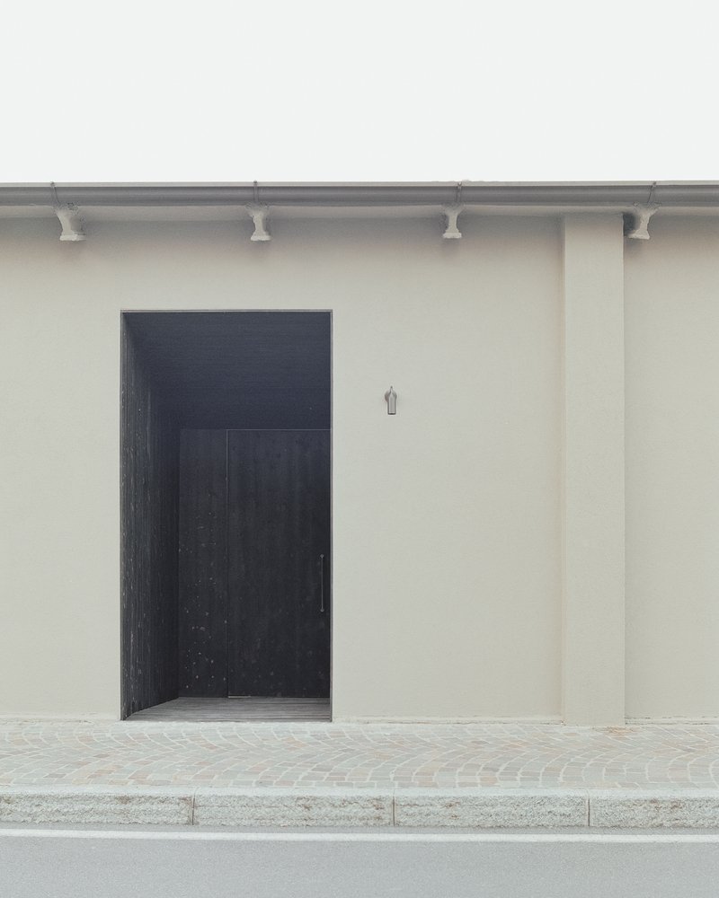 Black timber entry door set into smooth stucco wall with decorative terracotta corbels at the roofline