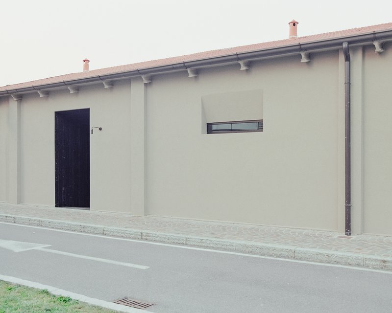 Street facade with recessed black timber door, narrow window and terracotta tile eaves under overcast sky