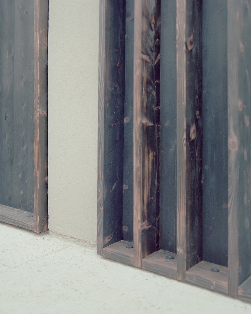 Close-up detail of charred timber battens meeting the rendered plaster at floor level