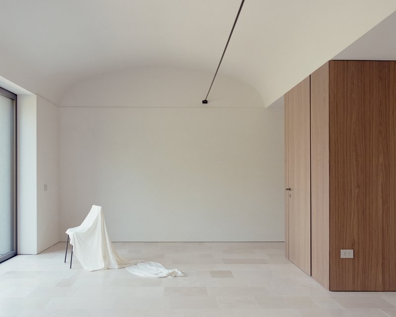 Interior room with vaulted ceiling, pale timber floor, walnut cabinetry and a draped cloth on a chair
