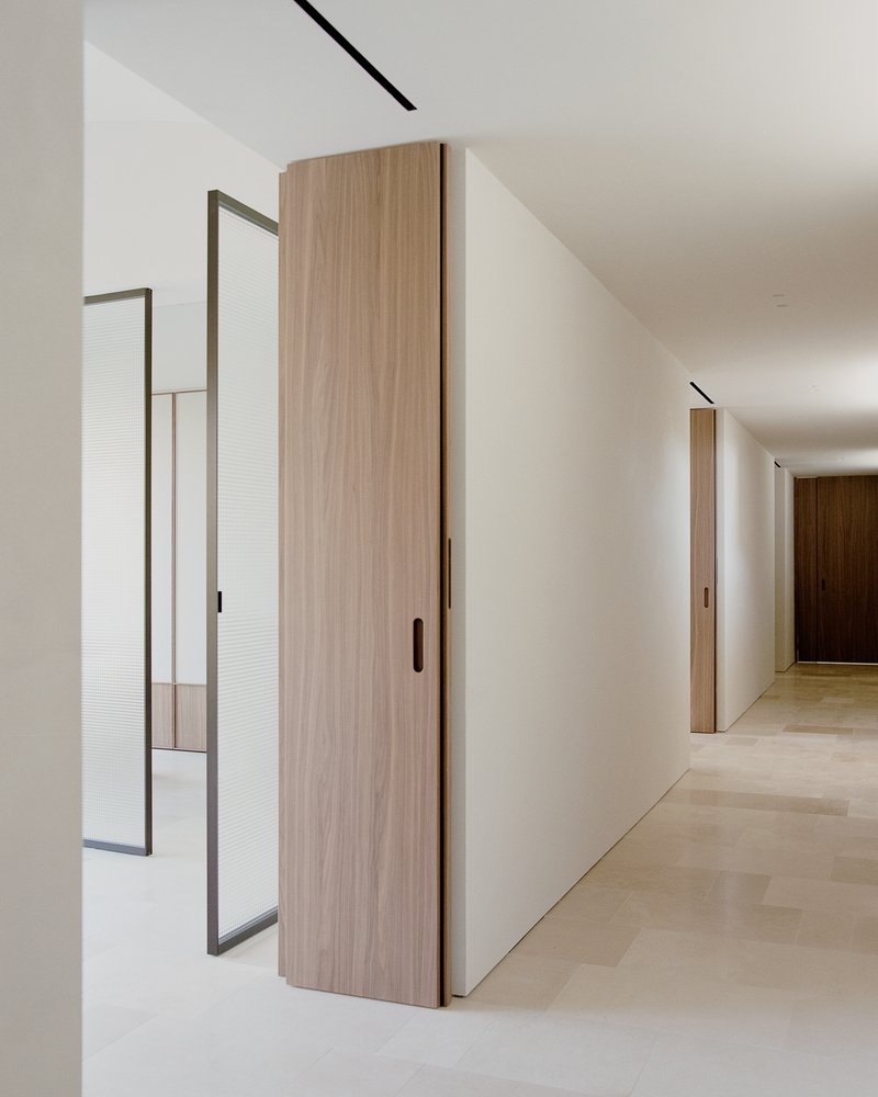 Corridor view showing walnut sliding doors, metal-framed reeded glass partition and recessed ceiling track
