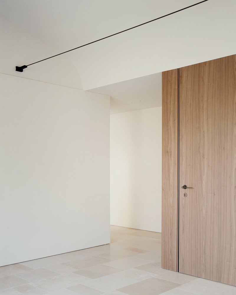 Interior corner with flush walnut door, white walls and linear black ceiling track lighting