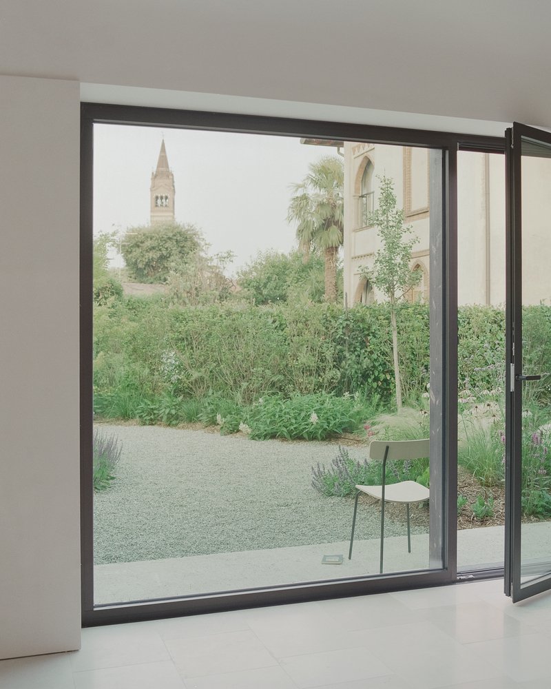 Open sliding glass door framing a view of a church bell tower beyond a garden path