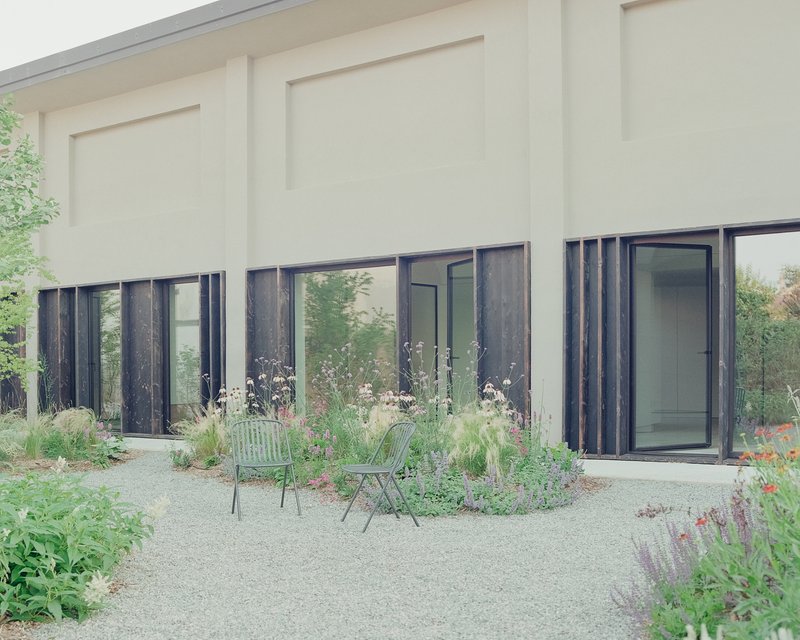 Garden courtyard with gravel path, planted beds and charred timber framed doors beneath a paneled facade
