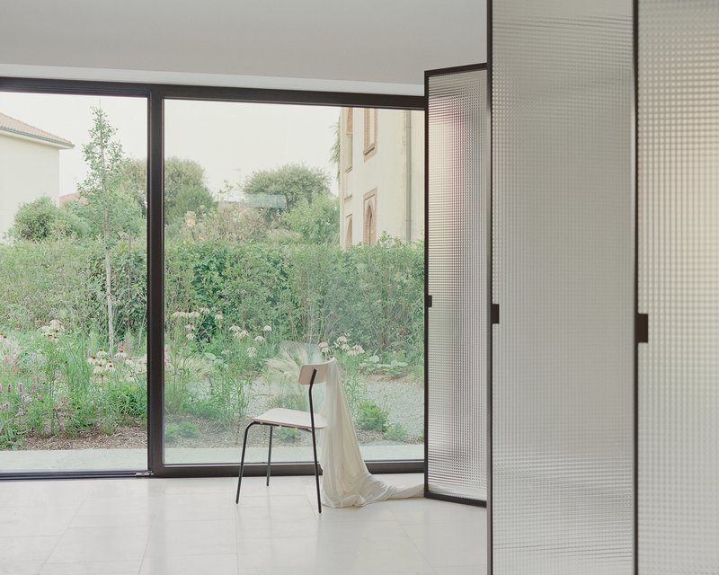 Corner window overlooking a garden with a single chair draped in fabric on polished floor