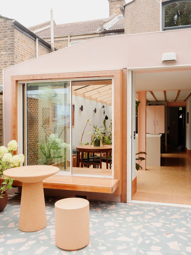 Open sliding glass doors revealing the dining area with exposed timber ceiling joists and potted plants