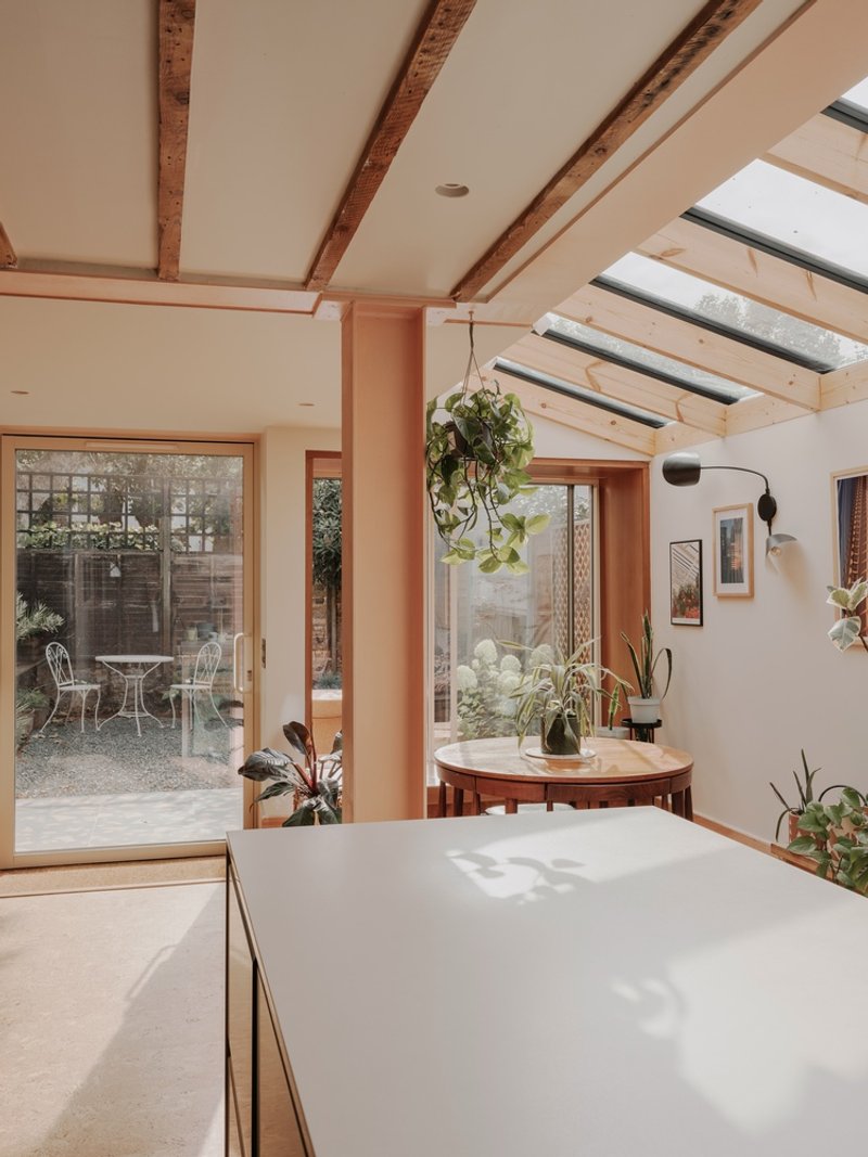 Kitchen island and dining table framed by timber columns with glazed doors opening to a gravel courtyard