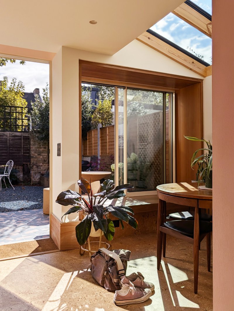Interior corner with timber-framed bay window overlooking courtyard and morning sunlight on cork flooring