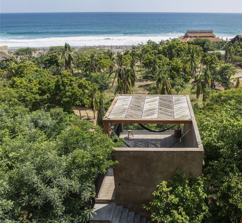Aerial view of the timber pavilion roof nestled among palms and tropical vegetation near the ocean