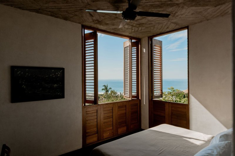 Bedroom with wooden louvered doors opening to an ocean view beneath a woven bamboo ceiling