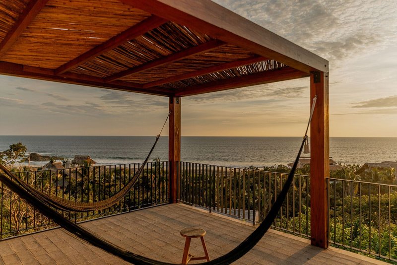 Upper terrace with timber pergola, metal railing and hammock overlooking the ocean at dusk