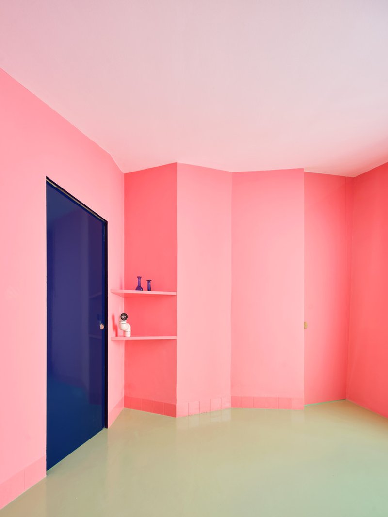 Corner shelving detail in pink room with blue door and pale green floor below