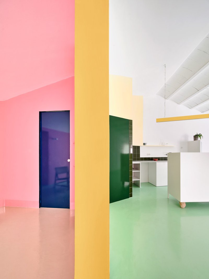 View through yellow partition showing pink floor meeting green floor with blue glass door at left