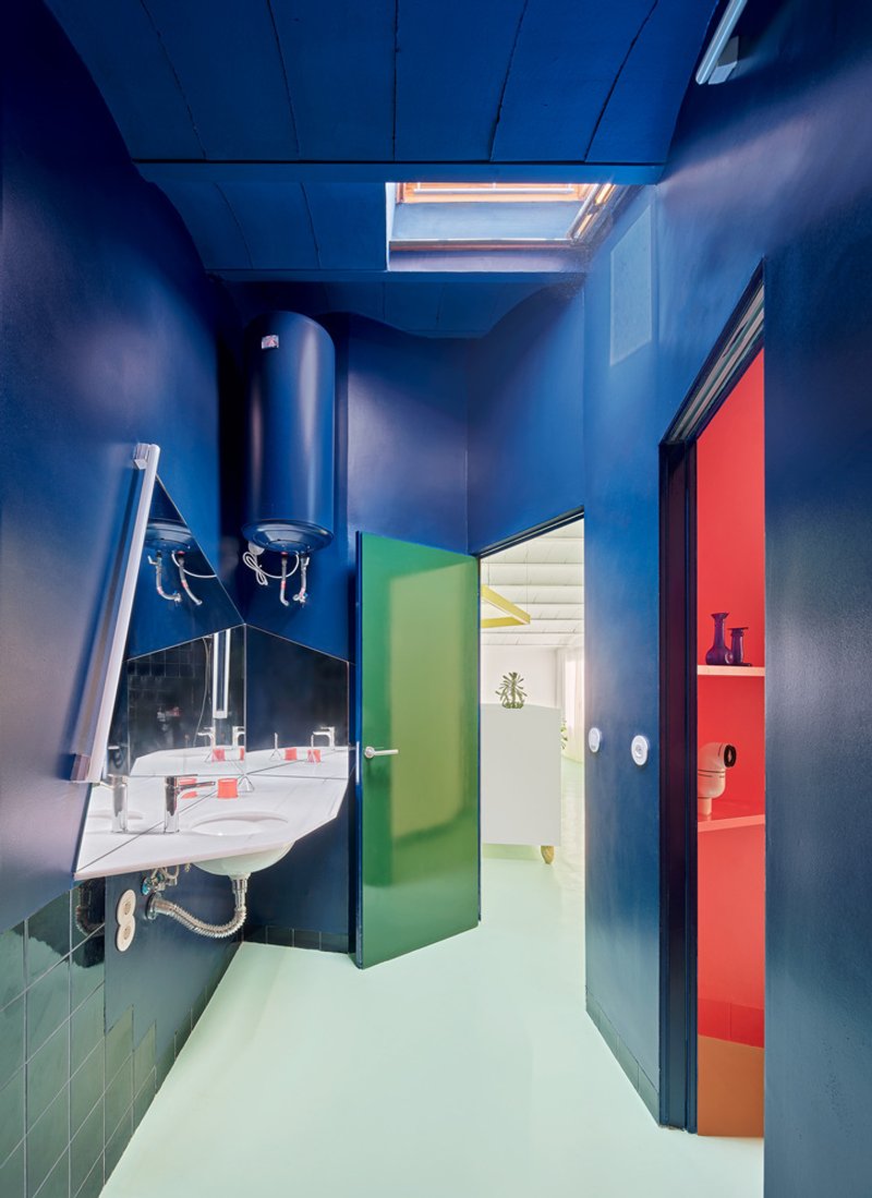 Bathroom with blue walls, pale green floor, and colored doors illuminated by skylight above