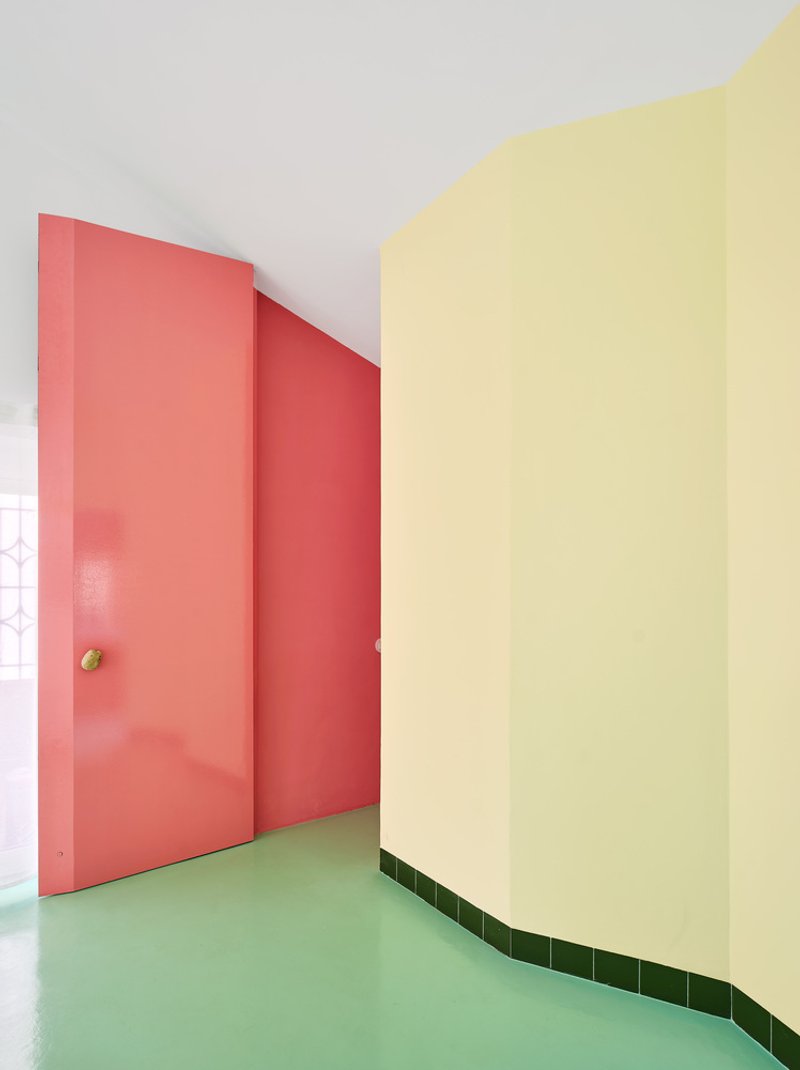 Hallway corner with pink door, yellow curved wall, and green tiled baseboard