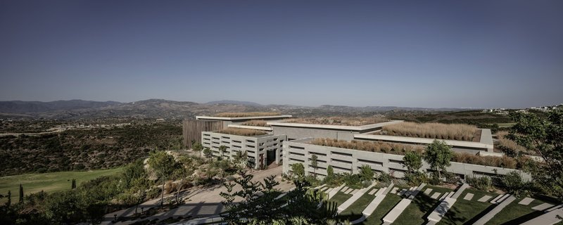 Horizontal louvered facade with rooftop terrace overlooking rolling hills under afternoon light