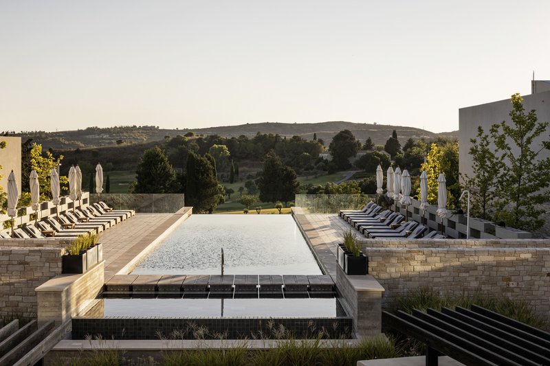Elevated pool deck with stone retaining walls and lounge chairs overlooking rolling hills at dusk