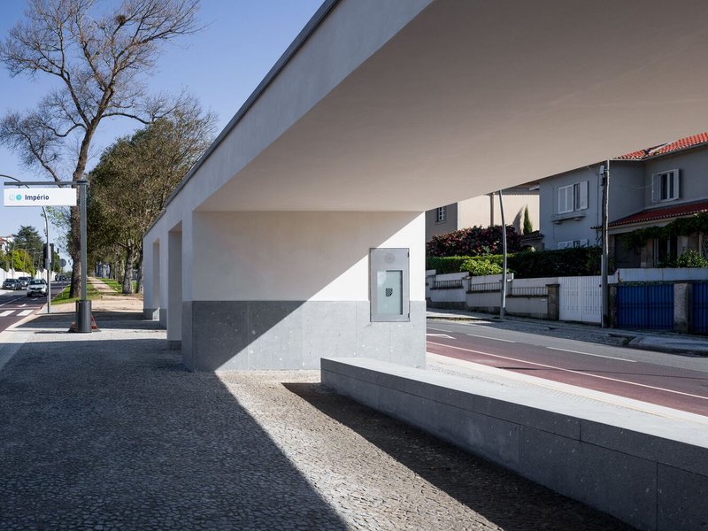 Street view of white cantilevered facade with grey base and bare trees along the sidewalk