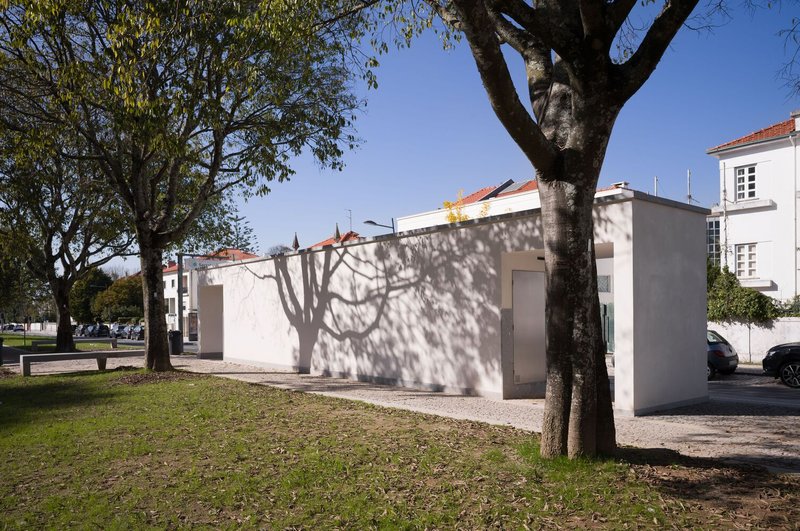 White pavilion structure casting tree shadows on its facade in the park setting