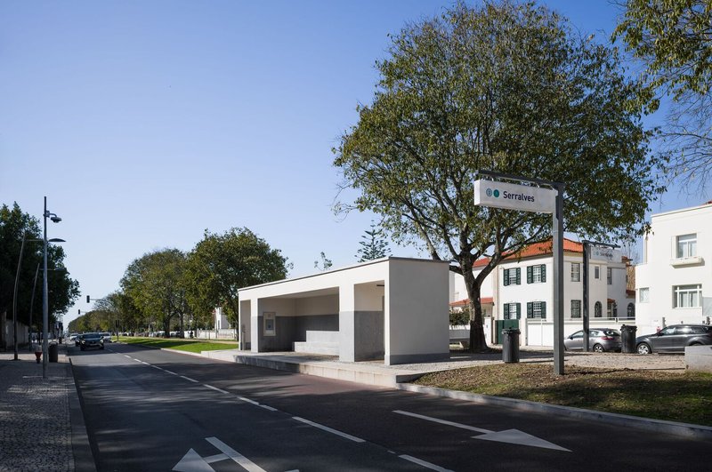 Elevated white pavilion structure with open sides framing a transit station sign and surrounding trees