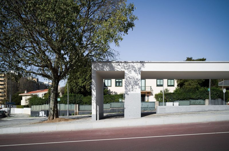 Street-facing white volume with large openings framing a residential building with orange roof