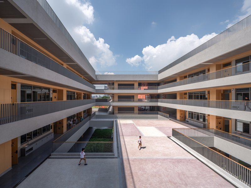 Courtyard view between concrete circulation galleries with timber screens and students crossing under afternoon clouds