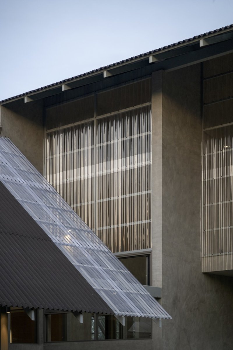 Concrete facade with vertical louvered screens and a translucent corrugated canopy at dusk